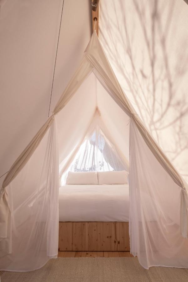 A cozy bed with white linens inside a tent with sheer white fabric drapes, allowing soft natural light to filter through—evoking the serene ambiance found in boutique hotels in Costa Brava.