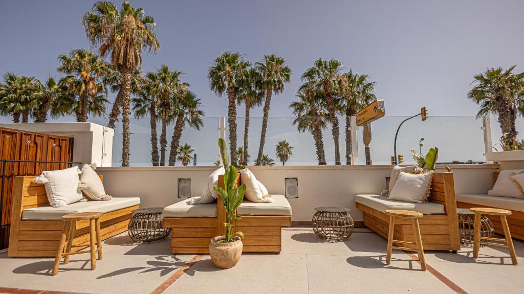 Adults-Only Hotels in Costa del Sol 5 Sunny outdoor patio with wooden benches, beige cushions, and potted plants. Palm trees line the background against a clear sky, creating a relaxing, tropical vibe—perfect for those seeking adult only hotels in Costa del Sol.