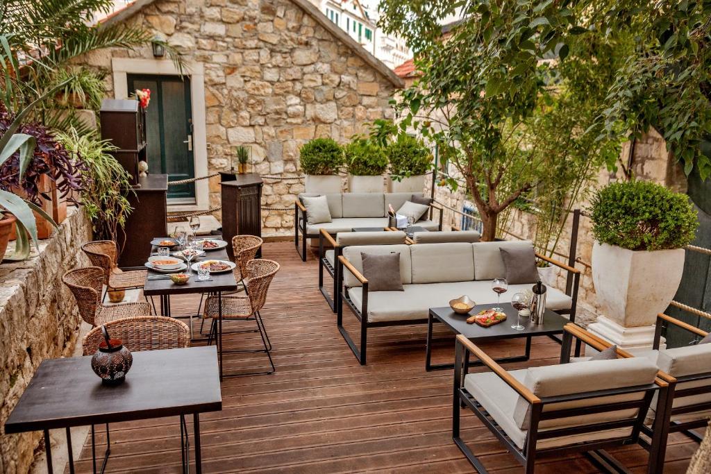 8 TOP Boutique Hotels in Split 33 A cozy outdoor patio with wooden flooring, modern sofas, and dining tables set with plates and drinks, surrounded by lush plants and a rustic stone wall—just the kind of charm you’ll find at boutique hotels in Split.