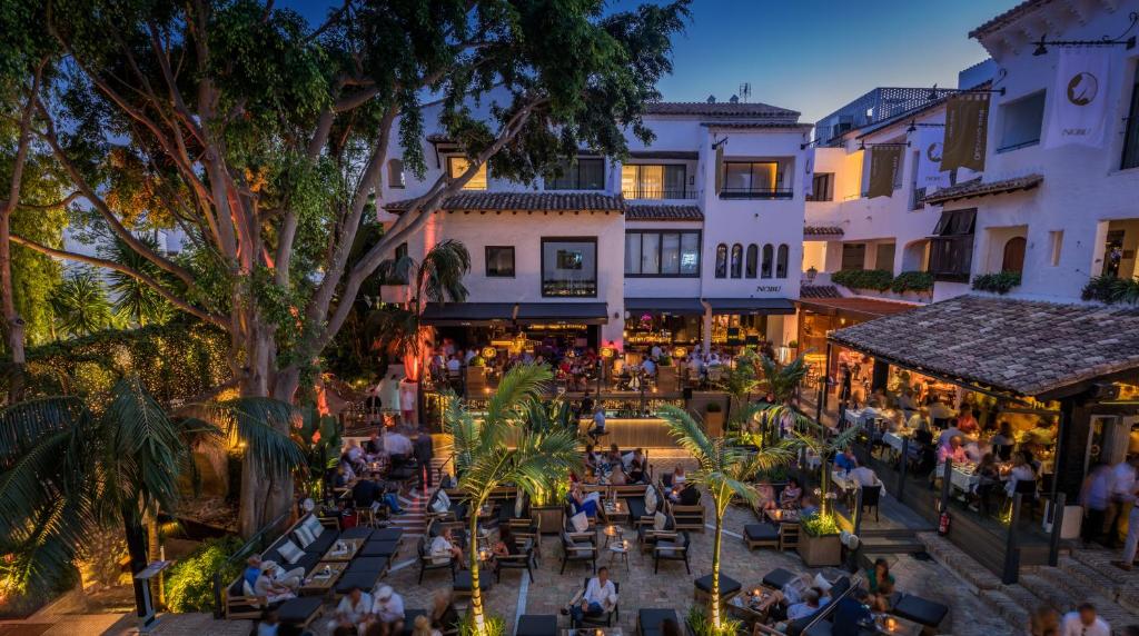 Adults-Only Hotels in Costa del Sol 14 An outdoor restaurant and bar with lush trees, string lights, and people dining in a relaxed, lively atmosphere—reminiscent of the inviting ambiance found at adult only hotels in Costa del Sol.