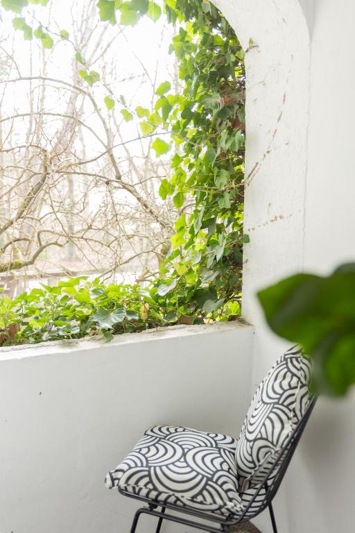 Authentic Boutique Hotels in Munich 11 A black metal chair with a patterned cushion sits on a white balcony—like those in boutique hotels in Munich—next to a curved opening framed with green ivy, overlooking bare tree branches outside.