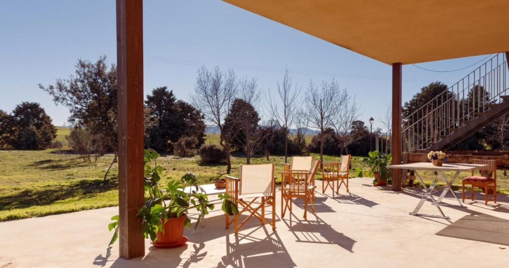25 Weekend Trips from Madrid Max. 2h Away 32 A covered outdoor patio with wooden chairs, potted plants, a small table, and a staircase offers a peaceful retreat—perfect for weekend trips from Madrid—overlooking a grassy yard and trees under a clear blue sky.