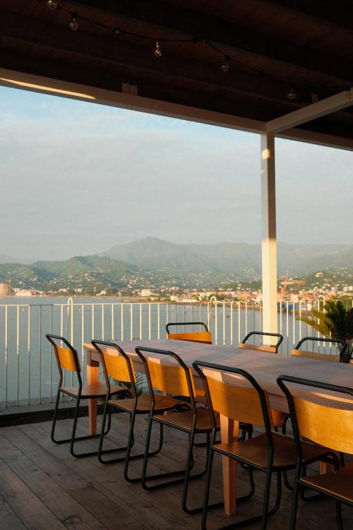 11 Unique Hotels in Georgia You Can't Miss! 40 A wooden table with several chairs sits on a covered outdoor terrace at one of the unique hotels in Georgia, overlooking a calm body of water and distant mountains under a clear sky.