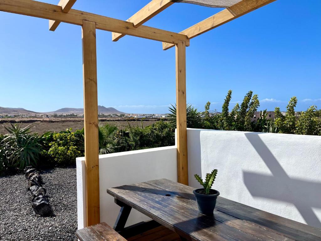 Adults Only Hotels in Fuerteventura 10 A wooden pergola shades a rustic picnic table with a small potted cactus on top. In the background, green plants, a stone path, and fields evoke the tranquil setting of adults only hotels in Fuerteventura under a clear blue sky.
