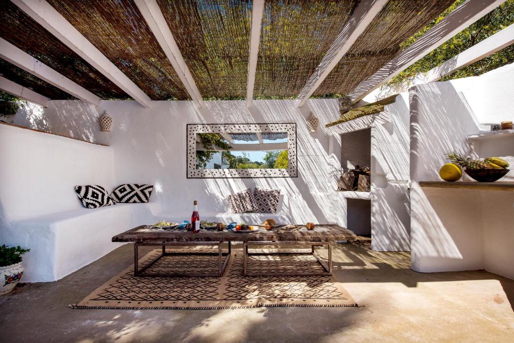 Adults-Only Hotels in Costa del Sol 37 A cozy outdoor patio with white walls, a wooden pergola, a rustic table set with food and wine—just like the inviting spaces found at adult only hotels in Costa del Sol—with patterned cushions, a mirror, and decorative accents in natural sunlight.