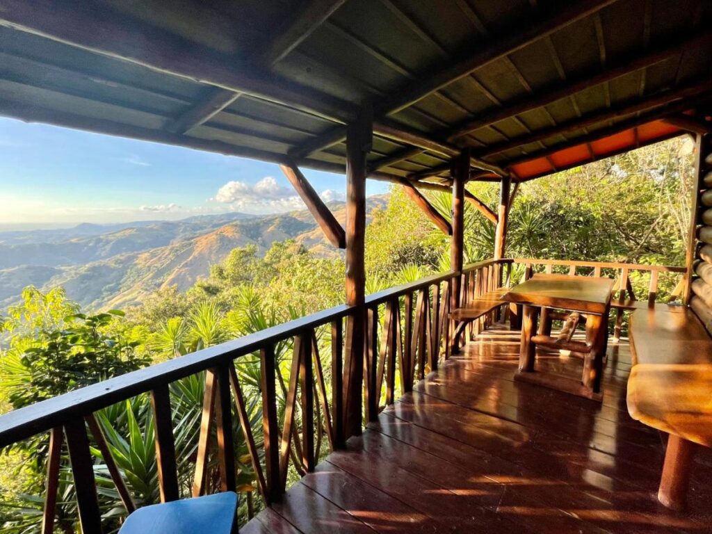 Unique Hotels in Costa Rica: Top Stays 21 Wooden porch with bench seating and a table overlooking a scenic mountain landscape—lush green trees, rolling hills, and clear blue sky—captures the charm found at unique hotels in Costa Rica.