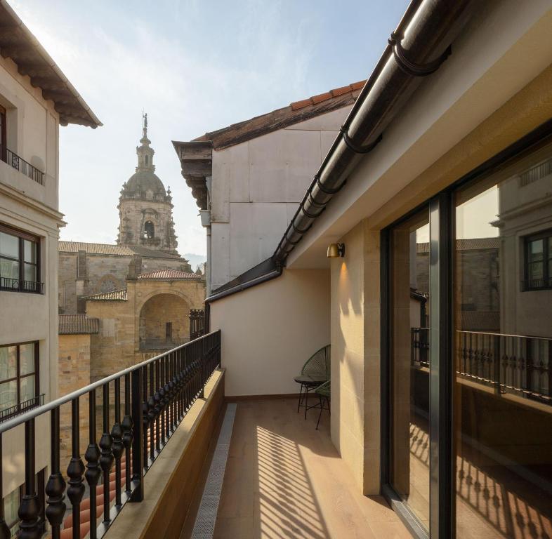 8 Unique Boutique Hotels in Bilbao Spain 3 A narrow balcony with a railing and a chair overlooks historic buildings, including a tall stone bell tower with a dome, under a clear sky—an ideal scene found at many boutique hotels in Bilbao.