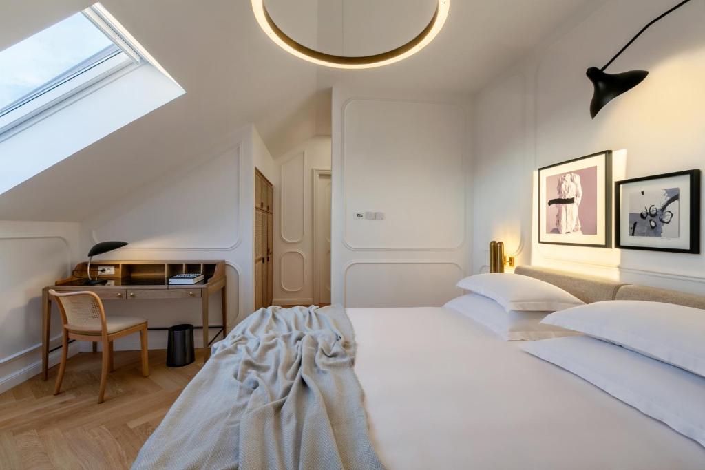 8 TOP Boutique Hotels in Split 11 A modern bedroom offers a cozy gray blanket on a neatly made bed, a wooden desk and chair under a skylight—perfect if you’re searching for where to stay in Split. White walls, wooden floors, and stylish decor complete the inviting space.