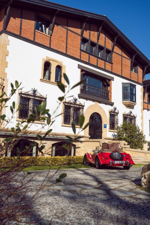 8 Unique Boutique Hotels in Bilbao Spain 30 A vintage red convertible car is parked on a cobblestone driveway in front of a large, elegant building with white walls—reminiscent of the chic style found at boutique hotels in Bilbao—under a clear blue sky.