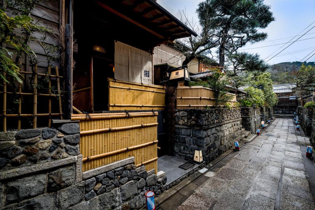 7 UNIQUE Ryokans in Gion Kyoto 6 Traditional Japanese street with stone walls and bamboo fences, lined with wooden houses and trees on a quiet, narrow walkway—lanterns and greenery enhance the serene charm, echoing the atmosphere of ryokans in Gion Kyoto.