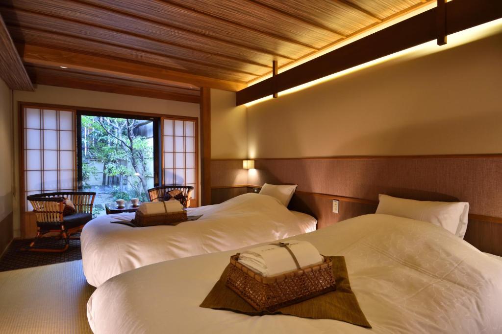 7 UNIQUE Ryokans in Gion Kyoto 26 A serene Japanese-style hotel room inspired by ryokans in Gion Kyoto, featuring two beds, woven baskets with towels, shoji screens, a small table with chairs, garden views through large windows, and warm ambient lighting.