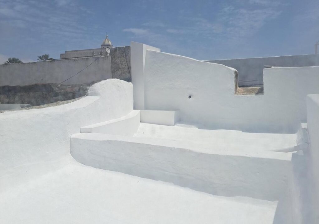 Unique Adults Only Hotels in Lanzarote 8 A sunlit rooftop with smooth, whitewashed walls and steps under a bright blue sky with scattered clouds—an idyllic scene reminiscent of Adults Only Hotels in Lanzarote. A dome and palm trees complete the relaxing atmosphere.