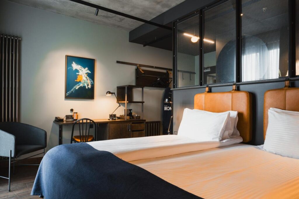 Where to Stay in Reykjavík: Top Guide 12 Modern hotel room with two neatly made beds, brown leather headboards, a blue throw blanket, and a desk—an ideal choice for where to stay in Reykjavik, offering comfort with a stylish workspace and separated sleeping area.