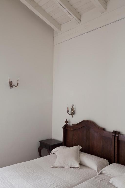 8 Unique Boutique Hotels in Bilbao Spain 26 A simple bedroom reminiscent of boutique hotels in Bilbao, featuring a wooden headboard, two single beds pushed together with white bedding, a pillow, a small dark nightstand, and candle-style sconces on light-colored walls.