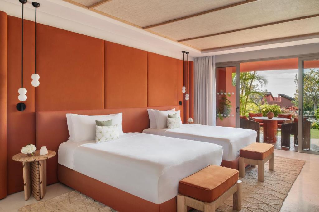 11 UNIQUE Boutique Hotels in Tenerife 48 A modern hotel room with two single beds, rust-colored accents, white bedding, wooden benches, a round side table, and a balcony overlooking greenery—perfect for those seeking boutique hotels in Tenerife.