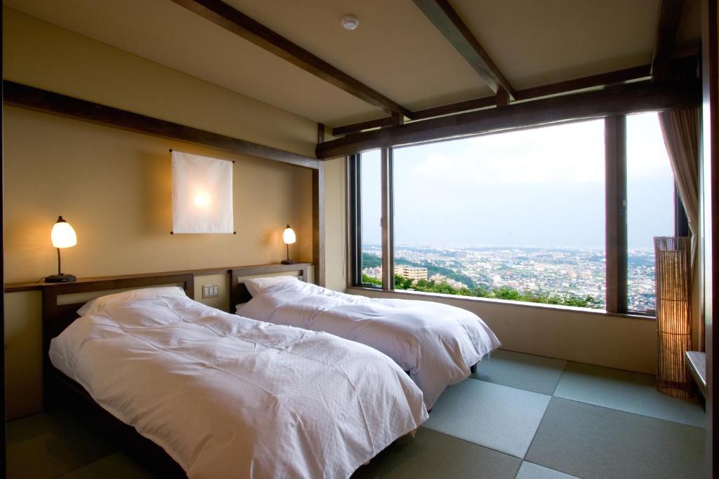8 BEST Ryokans in Osaka 28 A serene room inspired by ryokans in Osaka, with twin beds, soft lighting, tatami mat flooring, and a large window offering a panoramic view of the cityscape and distant mountains.