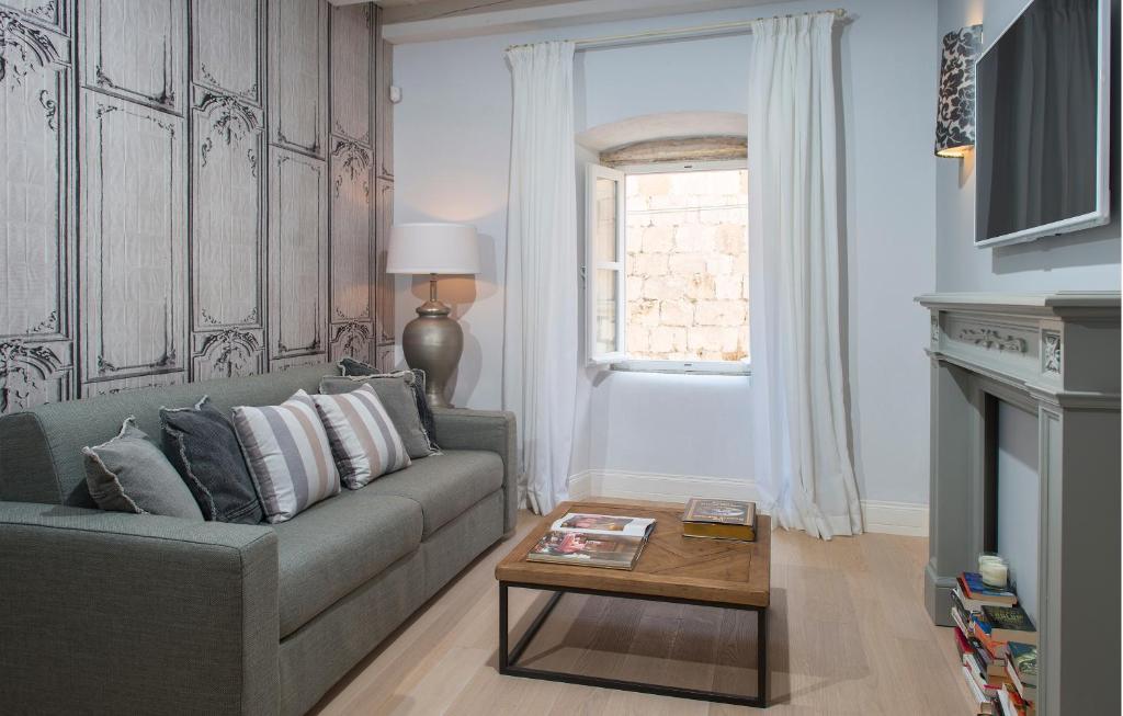 Most Unique Boutique Hotels in Dubrovnik 30 A modern living room with a grey sofa, striped and solid pillows, a wooden coffee table with books, cozy lighting reminiscent of boutique hotels in Dubrovnik, a window with white curtains, and a wall-mounted TV above a decorative fireplace.