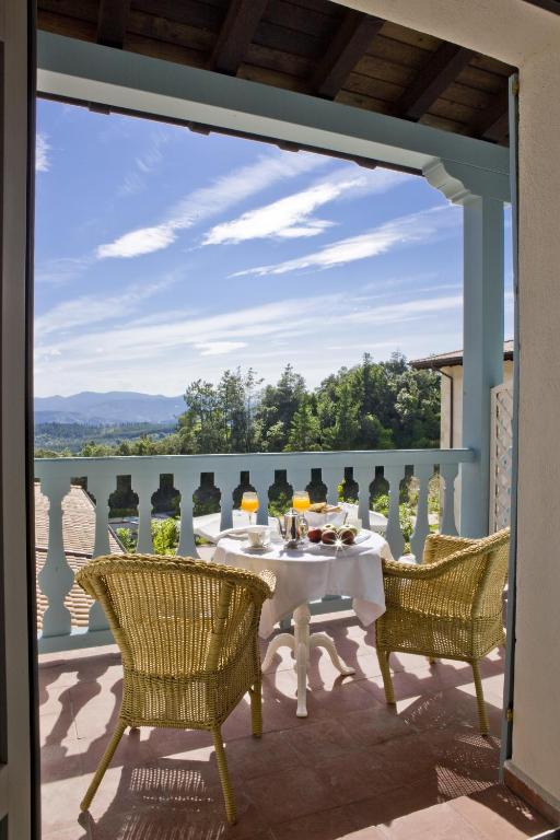 8 Unique Boutique Hotels in Bilbao Spain 19 A small balcony at one of the boutique hotels in Bilbao features two wicker chairs and a round table set for breakfast, with orange juice, coffee, and stunning views of green trees and distant mountains under a blue sky.