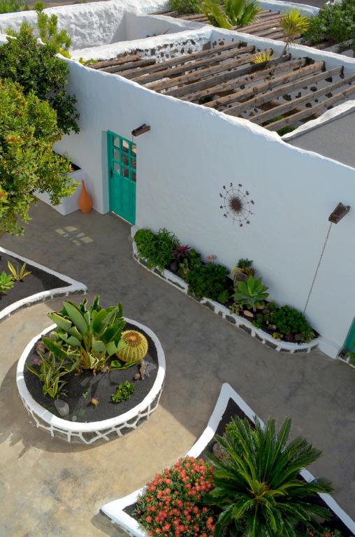 Unique Adults Only Hotels in Lanzarote 15 A view of a white-walled courtyard at one of the Adults Only Hotels in Lanzarote, featuring green doors, lush potted plants, raised garden beds, and a sunburst wall decoration under a partially covered pergola roof.
