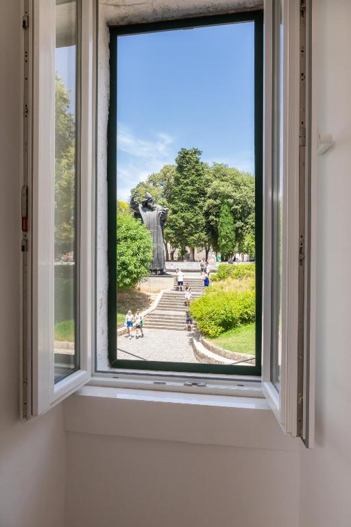 Where to Stay in Split: Hotel & Areas Guide 23 View through an open window showing a park with green trees, a pathway, people walking, and a tall dark statue on a stone pedestal under a blue sky—a scene reminiscent of Where to Stay in Split guides.