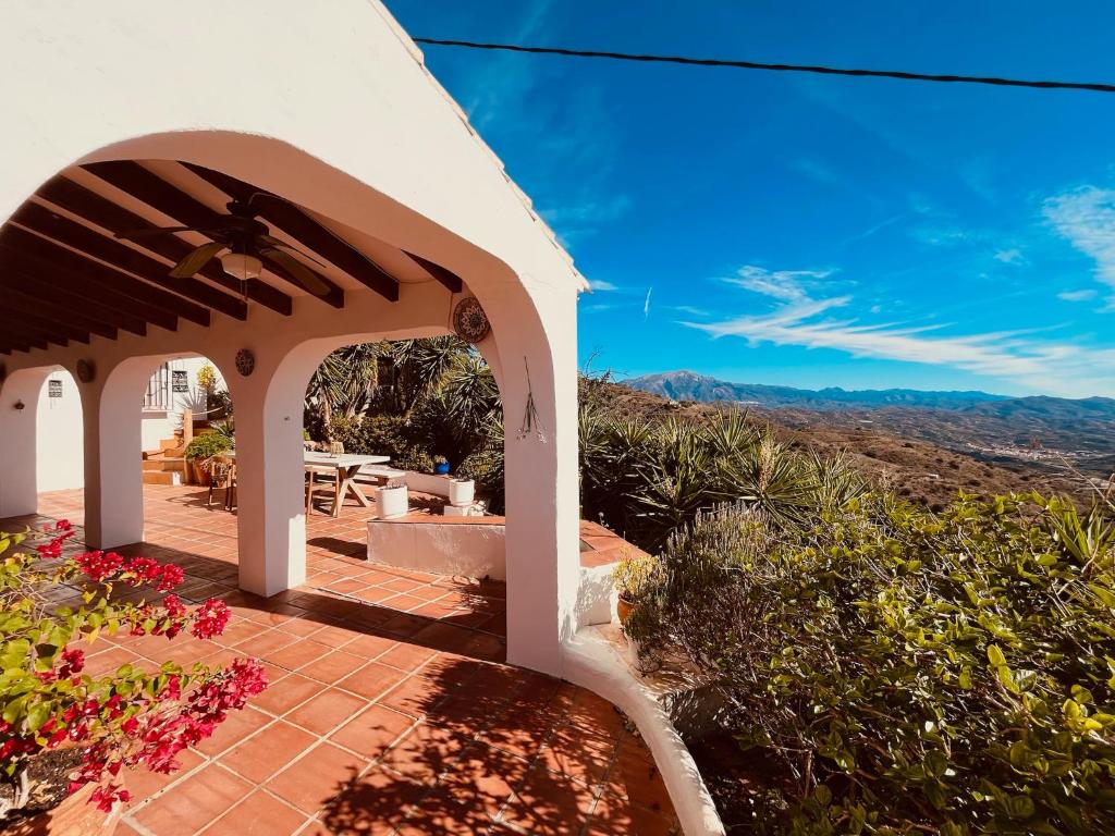 Adults-Only Hotels in Costa del Sol 34 A white stucco house with arches and terracotta tiles overlooks a scenic mountain landscape, much like the serene retreats found at adult only hotels in Costa del Sol, surrounded by lush greenery and colorful flowers.