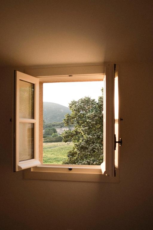 11 Unique Places to Stay in Provence 13 An open window in a beige wall reveals a view of a green field, a tree, and a distant hill under soft natural light—perfect for those seeking unique places to stay in Provence.