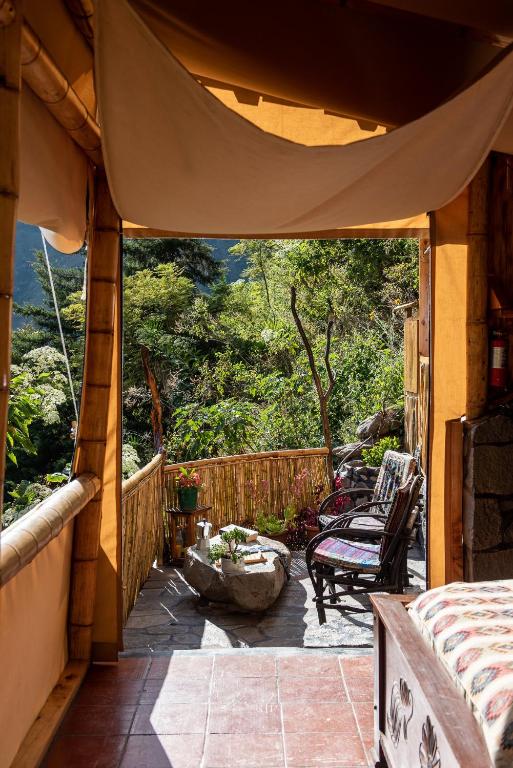 8 UNIQUE Places Where to Stay in Lake Atitlán 23 A rustic bamboo-framed doorway opens to a sunlit terrace with wicker chairs, a stone table, potted plants, and a lush green forest backdrop—an inviting spot if you're wondering where to stay in Lake Atitlan.