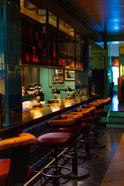 15 Best Boutique Hotels in London, UK 48 A cozy bar with padded red stools lined up along a polished counter, soft lighting, glassware, and small lamps—a stylish, warmly-lit interior reminiscent of the lounges found in boutique hotels in London.