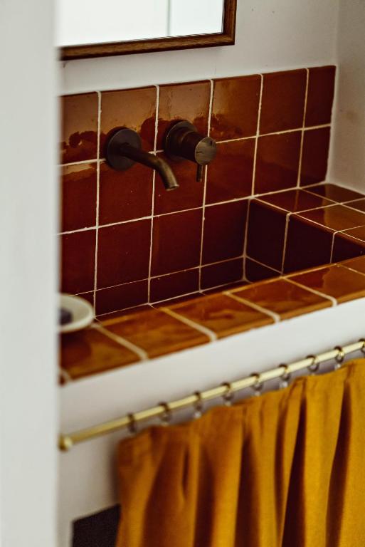11 Unique Places to Stay in Provence 12 A brown tiled bathroom sink with a wall-mounted faucet, a soap dish to the left, and a mustard yellow curtain below—a charming detail often found in unique places to stay in Provence.