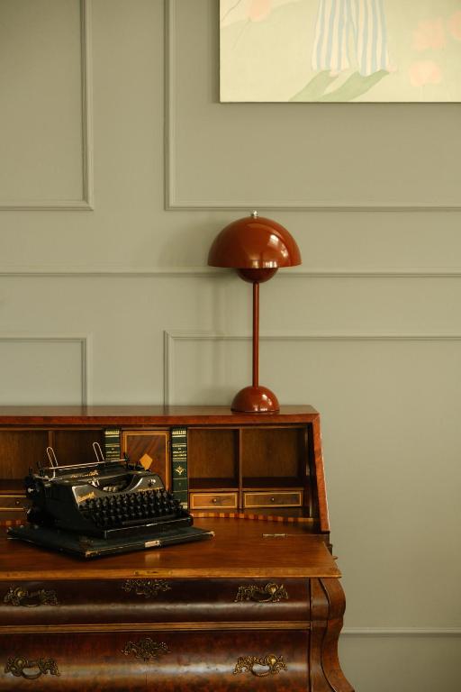 11 Unique Hotels in Georgia You Can't Miss! 24 A vintage wooden desk with an old-fashioned typewriter, green books, and a brown retro lamp sits against a paneled gray wallāevoking the charm found in unique hotels in Georgia, with part of a painting visible above.