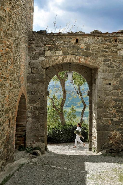 7 Best Agriturismos in Tuscany 9 A person in white walks through a stone archway of an old building, reminiscent of the best agriturismos in Tuscany, with trees and a blue lake visible in the background under a cloudy sky.