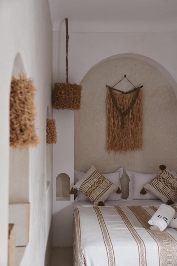 12 Charming Budget Riads in Marrakech 35 A cozy bedroom with neutral tones, featuring a bed with patterned pillows and blanket, woven wall art, and natural fiber lampshades—evoking the bohemian, earthy style often found in budget riads in Marrakech.