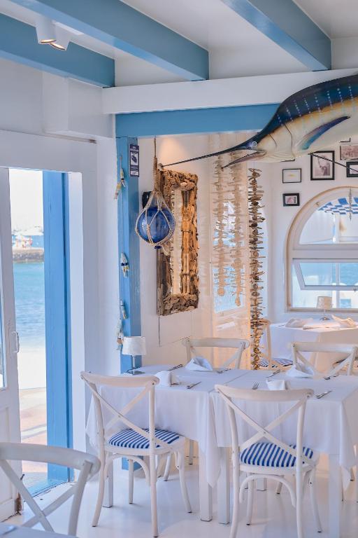 Adults Only Hotels in Fuerteventura 23 Bright, coastal-themed restaurant interior with white and blue decor, white chairs and table, nautical wall art including a large mounted fish—perfect for guests from adults only hotels in Fuerteventura—with sea views through window and glass door.