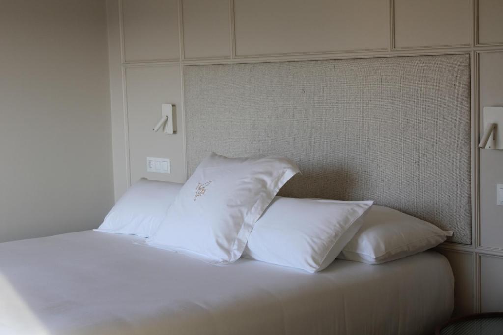 A neatly made bed with white sheets and a decorative pillow stands against a beige upholstered headboard, evoking the cozy elegance often found in boutique hotels in Asturias, beneath minimalist sconces on a light-colored wall.