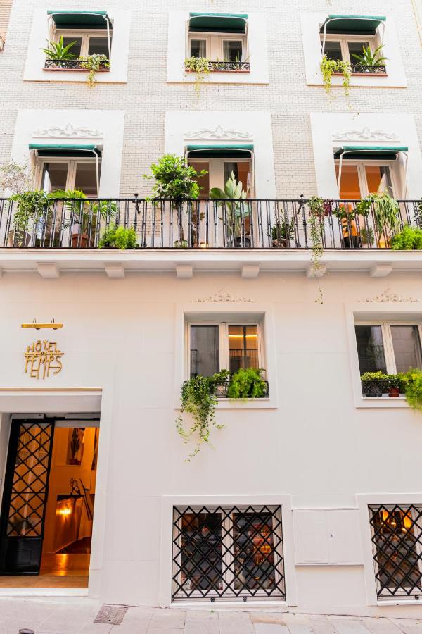 Where to Stay in Madrid: 14 Best Hotels 42 A three-story building with white walls, green awnings, and windows adorned with potted plants—Hotel Temps is an inviting choice for those wondering where to stay in Madrid first time, with a welcoming entrance marked by a lit sign above the door.