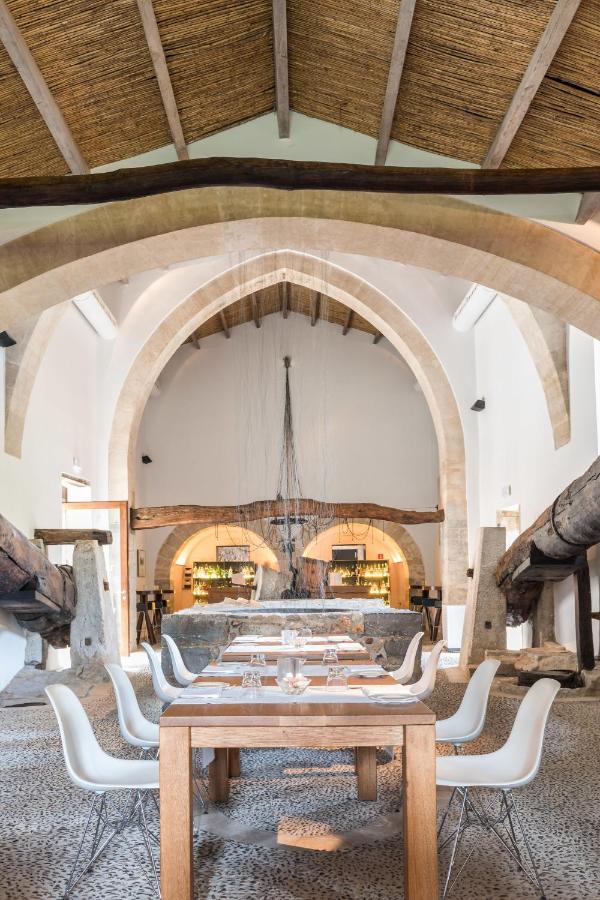 Unique Agroturismos in Mallorca 37 A modern dining area with white chairs and wooden tables sits inside a spacious room with arched stone ceilings, exposed beams, and rustic decor, echoing the unique charm of agroturismos in Mallorca.