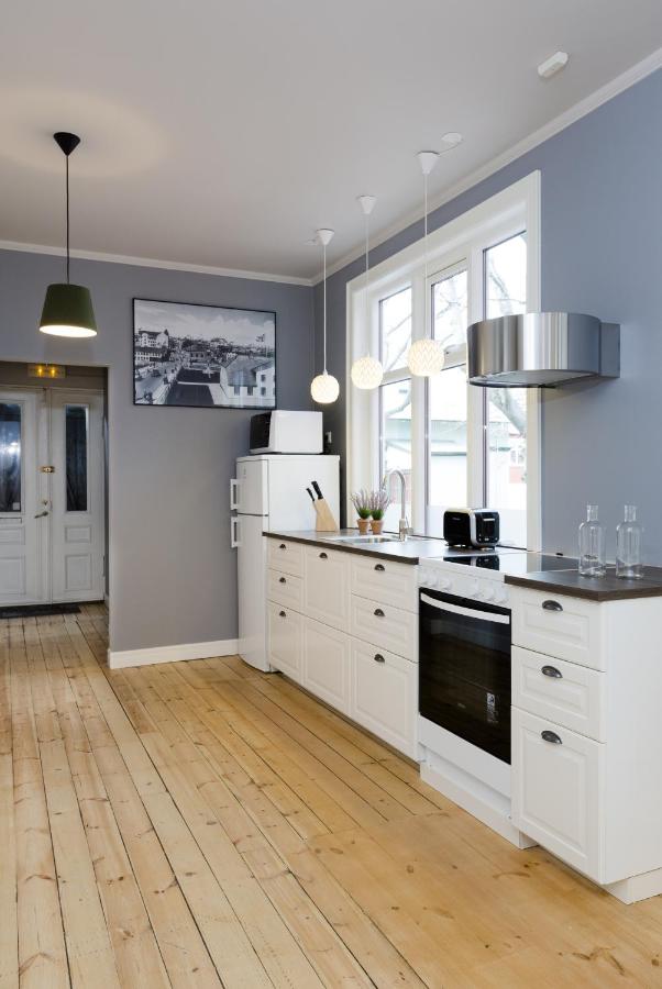 Where to Stay in Reykjavík: Top Guide 19 Modern kitchen with white cabinets, wooden floor, gray walls, and large windows—just the kind you might find when searching where to stay in Reykjavik. Three pendant lights illuminate the counter; appliances include oven, refrigerator, toaster, and range hood.