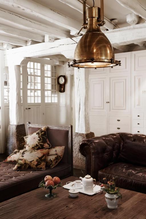 8 Unique Boutique Hotels in Bilbao Spain 28 A cozy living room inspired by boutique hotels in Bilbao, with leather sofas, floral cushions, a wooden coffee table set with a teapot and cups, a bowl of apples, a plant, white paneled walls, a vintage clock, and a large brass pendant lamp overhead.