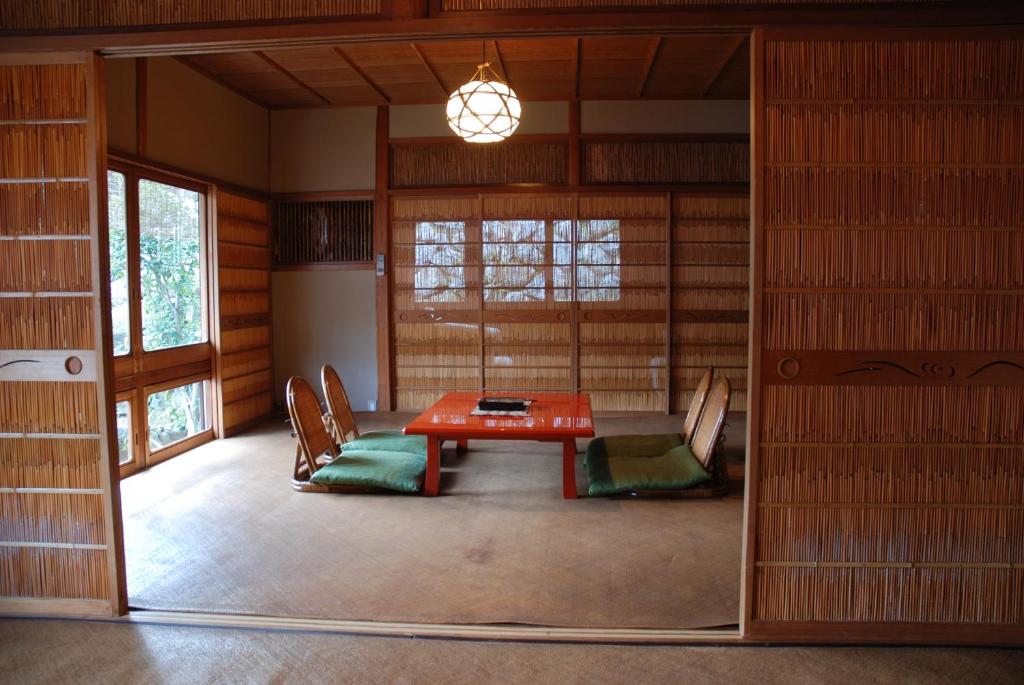 7 UNIQUE Ryokans in Gion Kyoto 16 A traditional Japanese room found in ryokans in Gion Kyoto, with tatami mats, a low red table, and four floor chairs with green cushions. Sliding shoji doors and wood paneling create a serene, minimalist atmosphere under a round ceiling light.