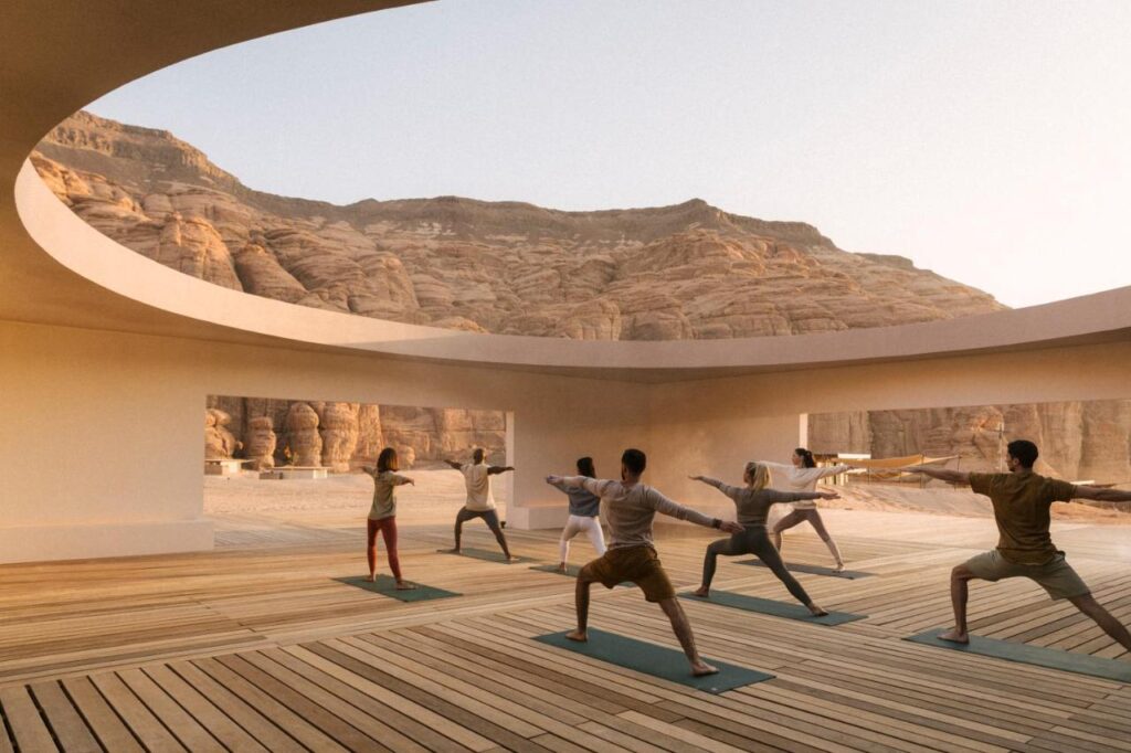 9 Best Hotels in Saudi Arabia: Unique Stays Across the Country 12 A group of people practice yoga on mats in an open, circular structure with wooden floors, surrounded by rocky desert mountains under a clear sky—an experience often offered at the best hotels in Saudi Arabia.