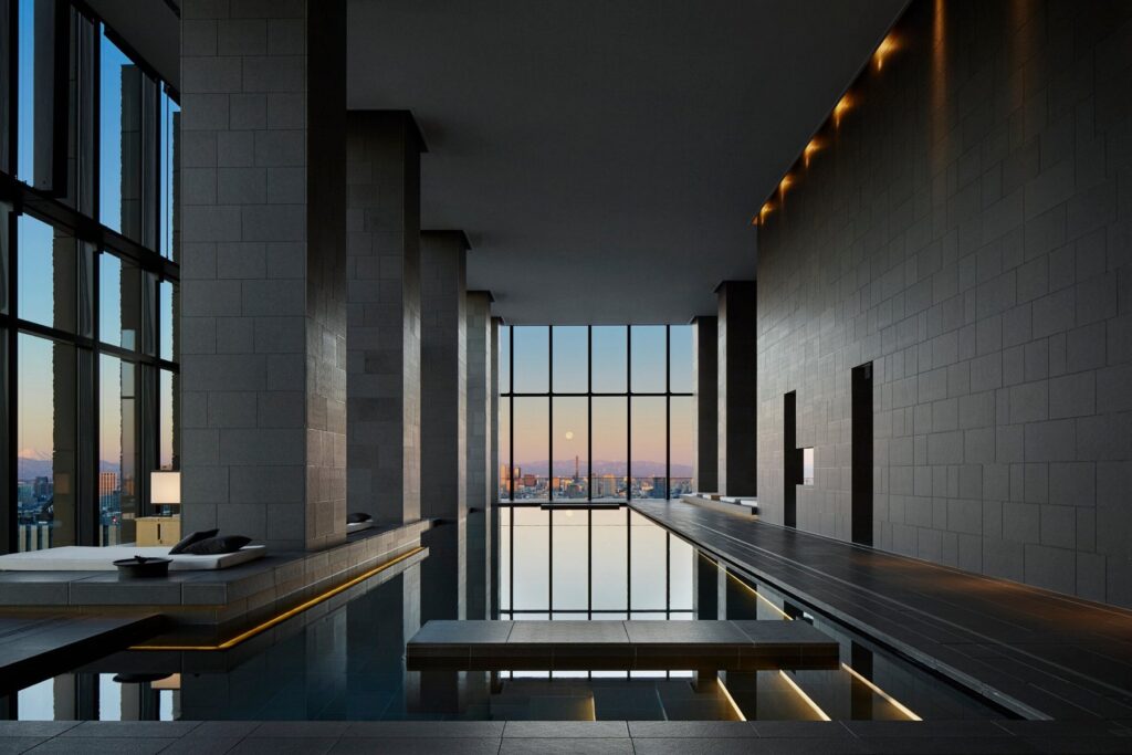 15 Unique Hotels in Tokyo: Coolest hotels 28 A modern indoor pool with clean lines, high ceilings, and tall windows offering a cityscape view at sunset; soft lighting accents the minimalistic, elegant design often found in unique hotels in Tokyo.
