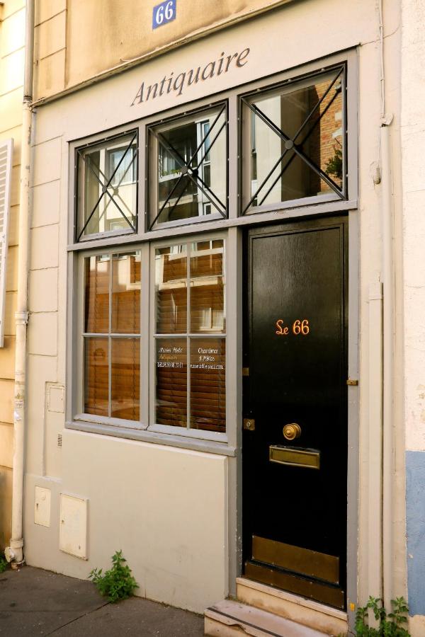 13 Unique Hotels in Paris for a Stylish Stay 13 A storefront with a black door and window above it, labeled Antiquaire and Le 66—hinting at an antique shop. The cream-colored building with a blue street number 66 sits among unique hotels in Paris, offering charm and character.