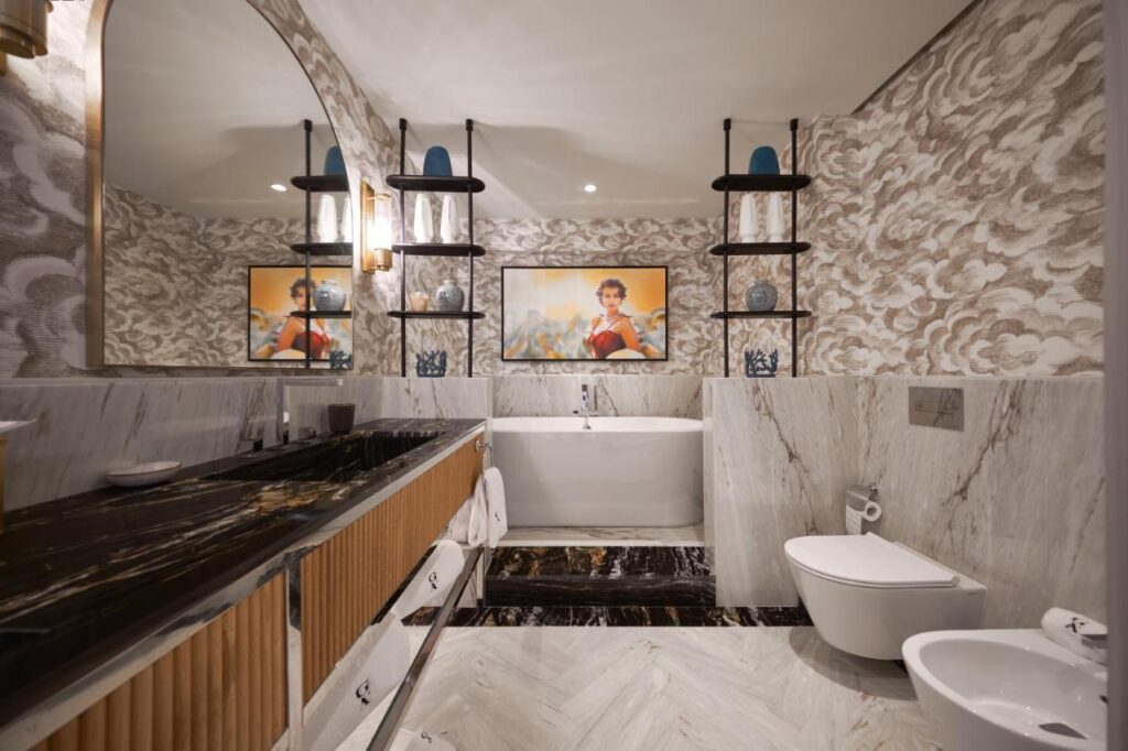 Top 12 Boutique Hotels in Porto, Portugal 7 Luxurious bathroom with marble walls and floors, a large bathtub, modern sink, toilet, and bidet—reminiscent of the refined style found in boutique hotels in Porto. Decorative shelves and ambient lighting complete this elegant atmosphere.