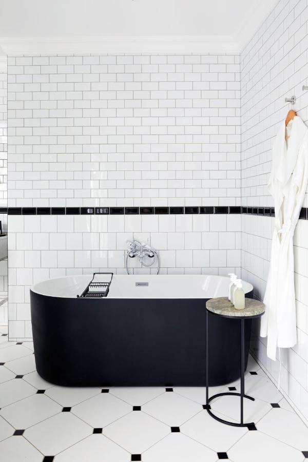 Unique Places to Stay in Cape Town 12 A modern bathroom with white subway tile walls, a black freestanding bathtub, a round side table with a soap dispenser, a robe hanging on the wall, and a tiled floor with black accents—one of the unique places to stay in Cape Town.