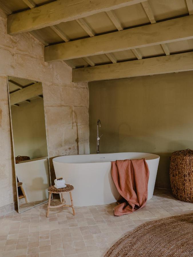 Unique Boutique Hotels in Menorca 21 A cozy bathroom reminiscent of boutique hotels in Menorca, featuring a freestanding white bathtub, a pink towel draped over the edge, a wicker laundry basket, a small wooden stool with items on it, and rustic beige walls and ceiling.
