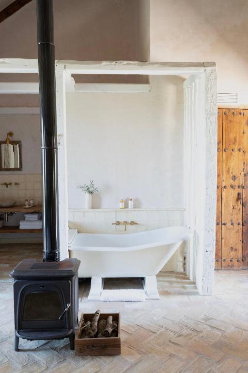 TOP 10 Luxury Hotels in Andalucía 11 A cozy bathroom reminiscent of luxury hotels in Andalucía features a vintage freestanding bathtub, a wood-burning stove with a chimney pipe, and a crate filled with firewood on a herringbone-patterned floor. Light streams in, creating a serene atmosphere.