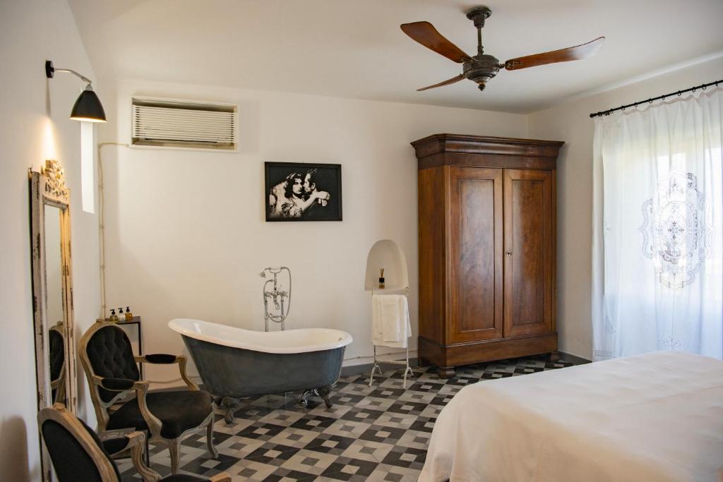7 Best Hotels in the Aeolian Islands 28 A bright vintage-style bedroom like those found in hotels in the Aeolian Islands, featuring a freestanding bathtub, ornate mirror, black-and-white checkered floor, wooden armoire, elegant chairs, ceiling fan, and bold black-and-white artwork.
