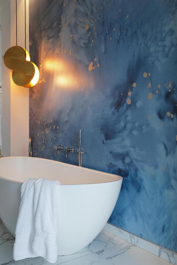 Unique Places to Stay in Cape Town 16 A modern bathroom with a white freestanding tub, a white towel draped over the side, marble flooring, blue abstract wall art, and two round pendant lights—perfect inspiration for unique places to stay in Cape Town.