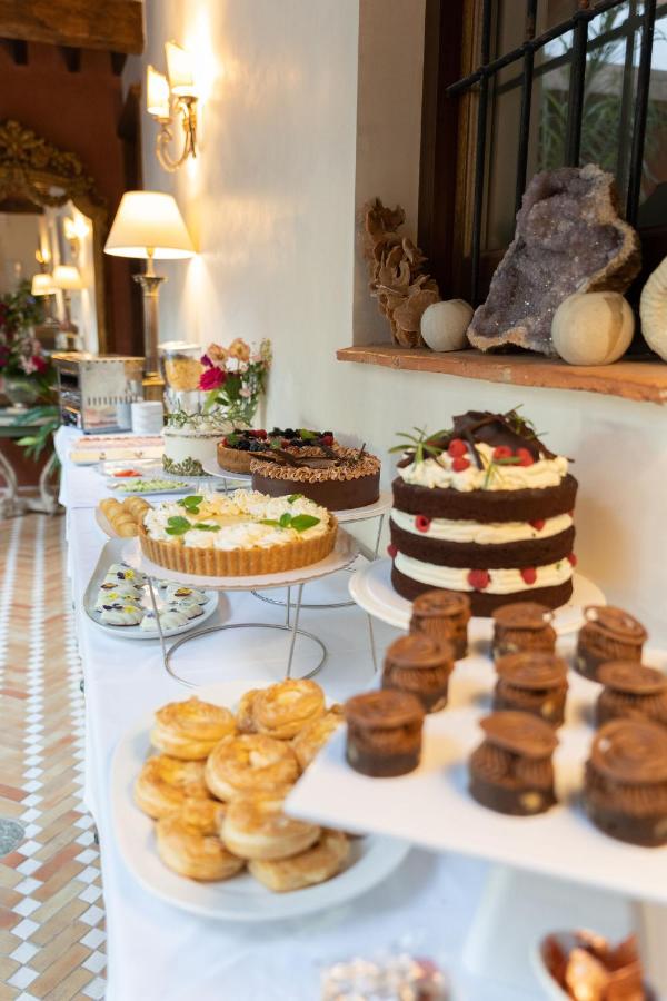 A dessert table with a variety of cakes, tarts, and pastries displayed on plates and stands, set against a warmly lit wall with decorative objects and flowers—echoing the charming ambiance of boutique hotels in Granada.