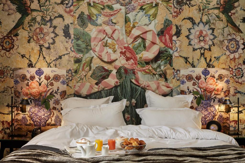 11 Unique Places to Stay in Provence 46 A luxurious bed with crisp white linens is set against a vibrant, floral-patterned wall in one of the unique hotels in Paris. Ornate lamps grace the bedside tables, while breakfast with drinks and pastries is elegantly served on the bed.